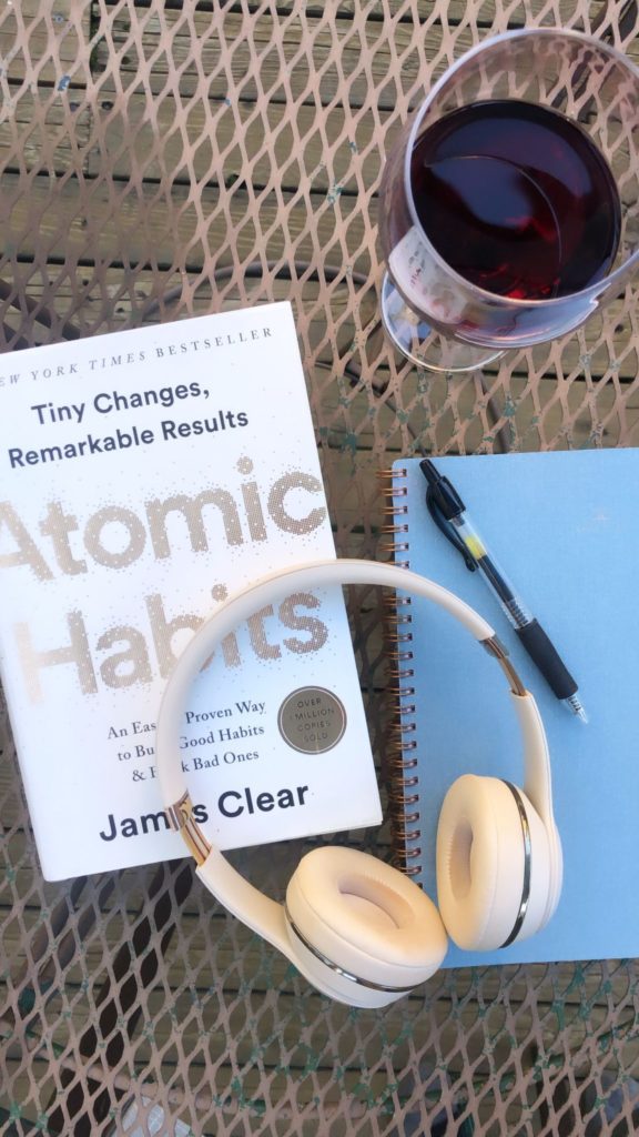Atomic Habits, wine glass, Beats headphones, notebook, and pen on a table